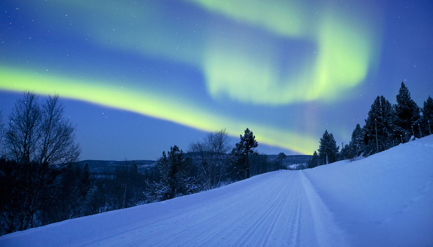 Finnland - Aurora borealis over a road through winter landscape, Finnish Lapland